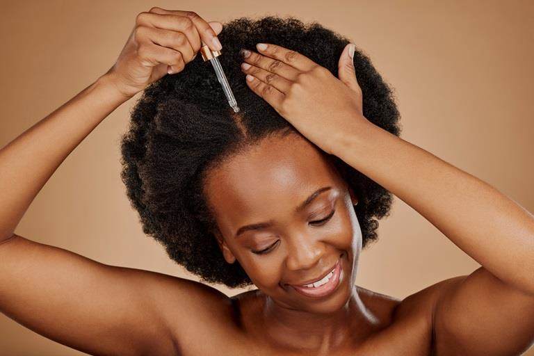 Young black woman with black natural hair applying serum to her scalp.